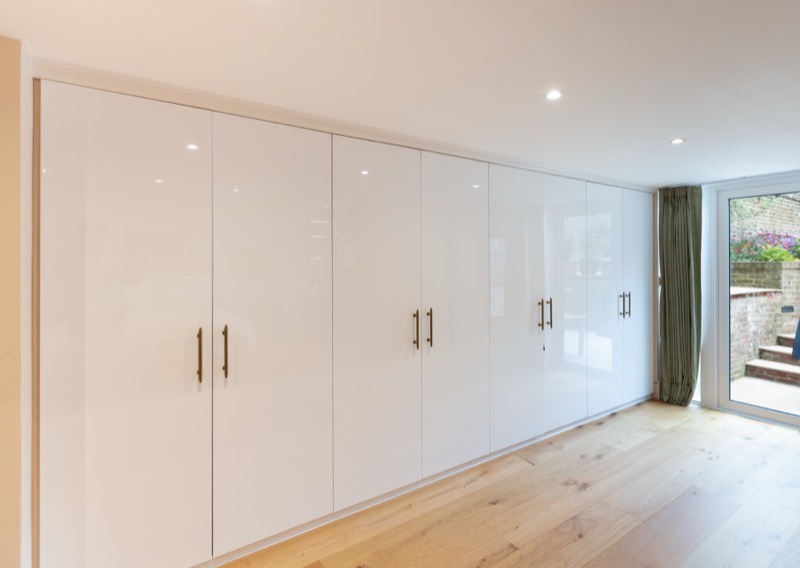 Floor-to-ceiling high-gloss fitted wardrobes with brass handles opening onto a garden terrace