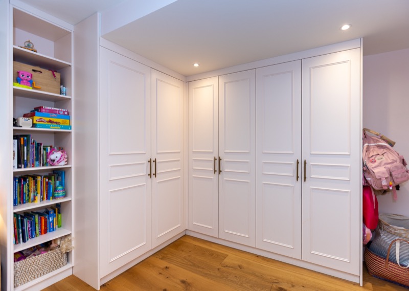 Bespoke panelled wardrobes in pale timber forming a full corner storage wall