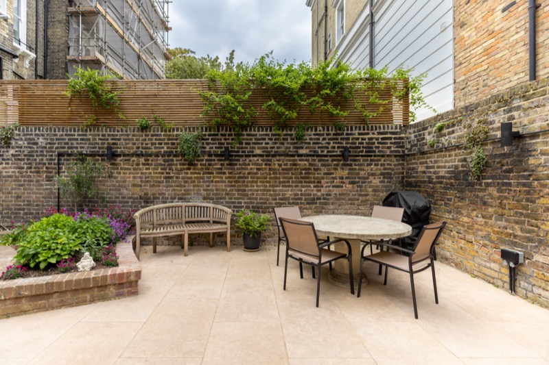 Walled patio garden with stone paving, slatted timber privacy screen, climbing greenery and outdoor dining set