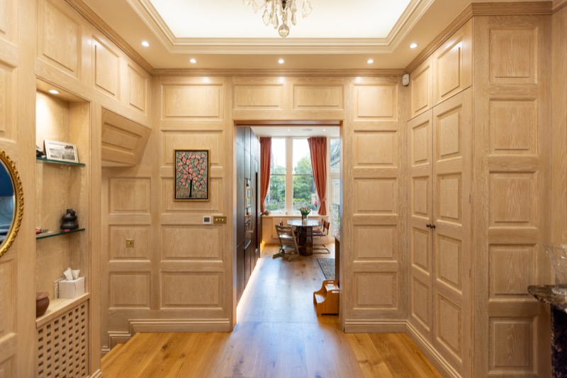 Oak-panelled hallway with leaded shelving niche leading through to a dining room beneath a crystal chandelier