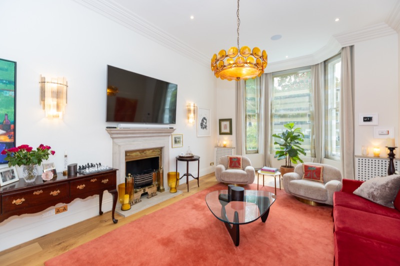 Reception room with carved fireplace, mounted television, crystal sconces and red velvet seating beneath ornate ceiling rose