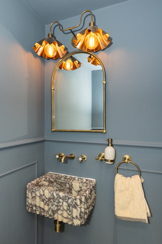 Bathroom basin in book-matched marble with ornate brass mirror, ruched copper sconces and blue panelling