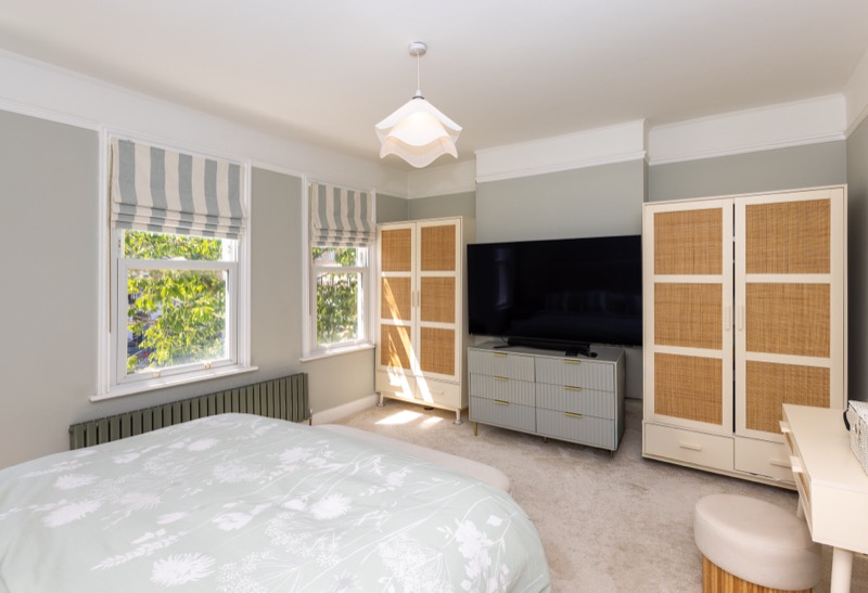 Bedroom with rattan wardrobes, striped Roman blinds, dressing chest and wall-mounted television