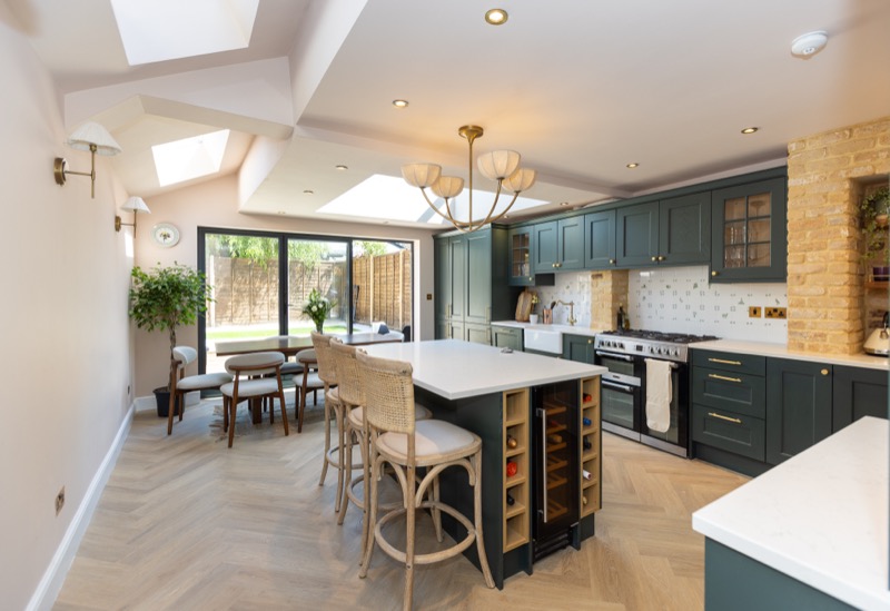 Open-plan Shaker kitchen with marble island, bar stools and bifold doors opening onto a garden under a skylight extension