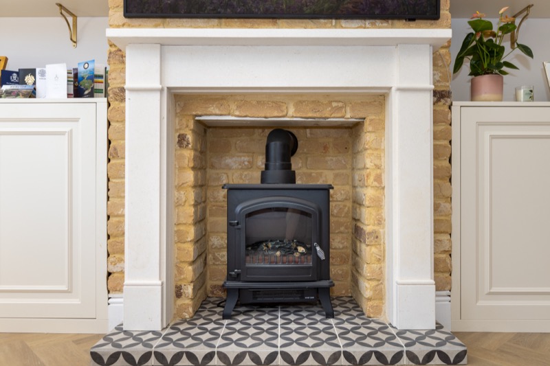 Cast-iron woodburner set in a stone fire surround with patterned tile hearth and exposed brick