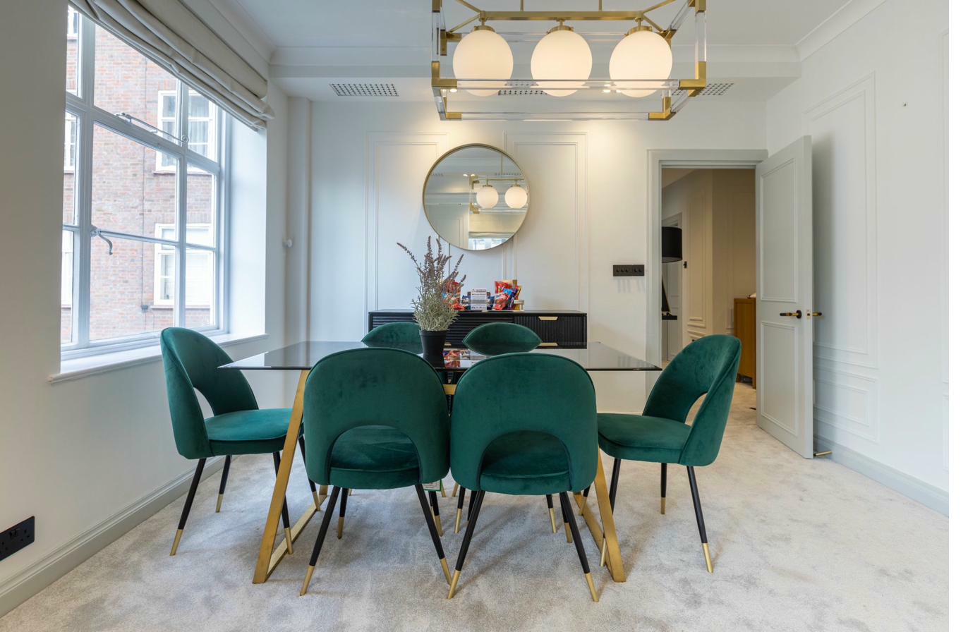 Elegant dining room with emerald chairs and round mirror